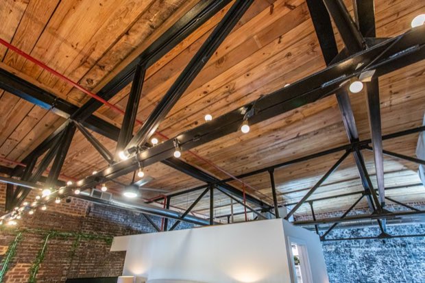 Timber plank ceiling and black steel roof trusses strung with cafe lights