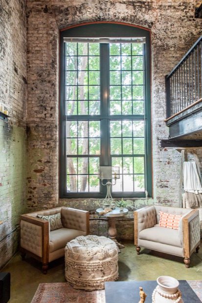 Two-storey arched factory window framed by exposed brick, with a pair of tufted chairs