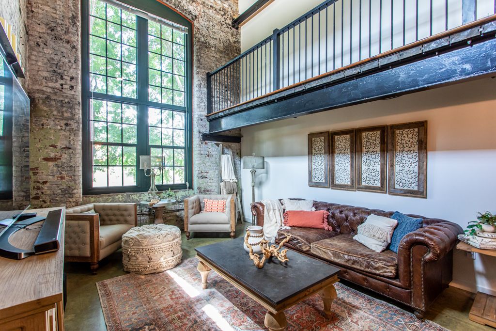 Living room with a leather Chesterfield beneath the arched factory window and mezzanine