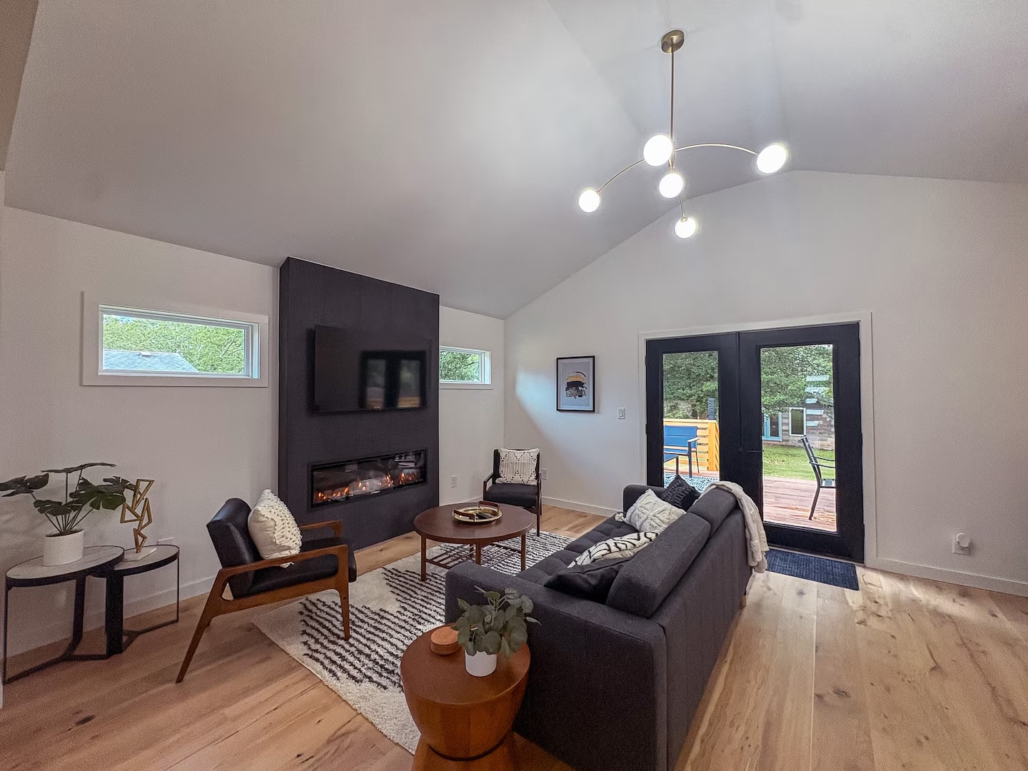 Vaulted living room with a linear fireplace, mid-century lounge chairs and French doors opening to the deck