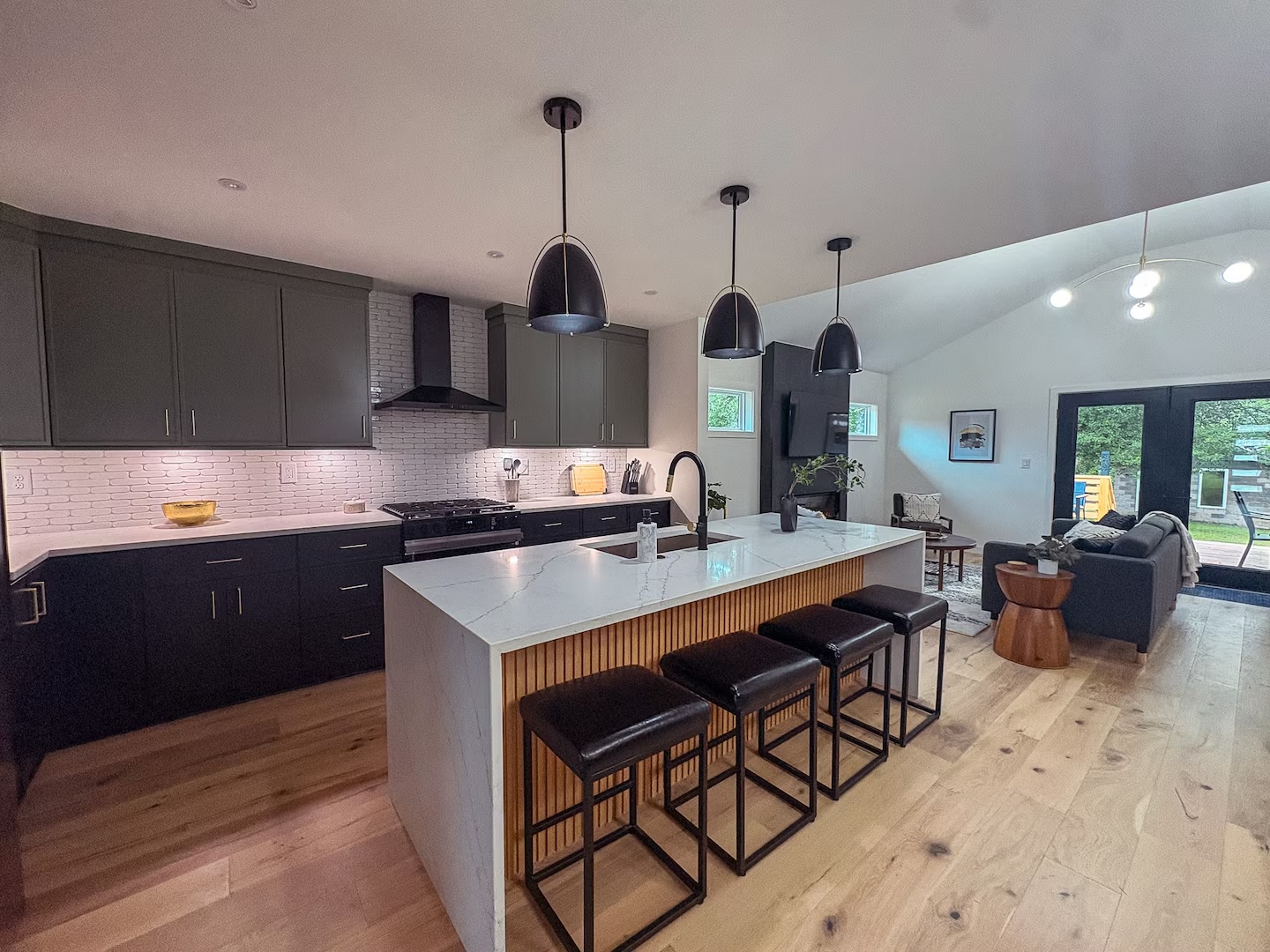 Kitchen with a marble waterfall island, bar seating and matte black pendants