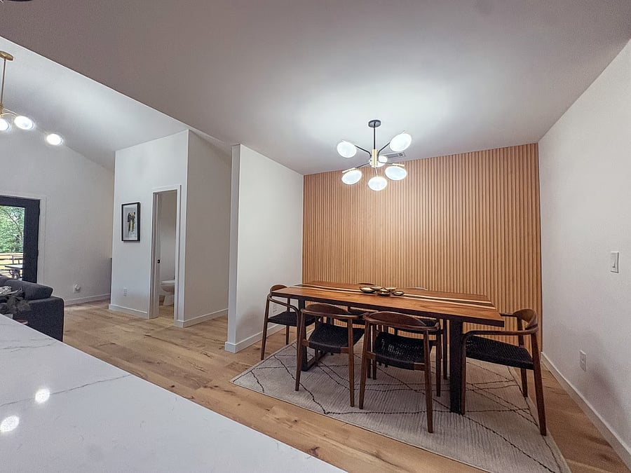 Dining area with a white oak slat wall and a six-globe modern chandelier