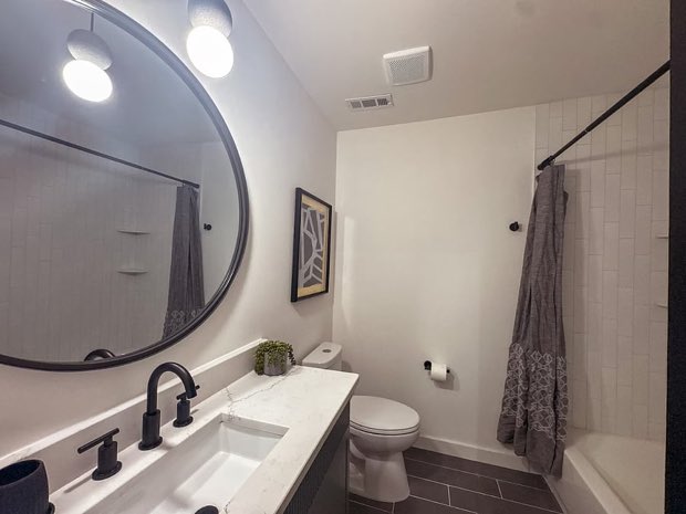 Full bathroom with a round mirror, quartz vanity and a tub-shower