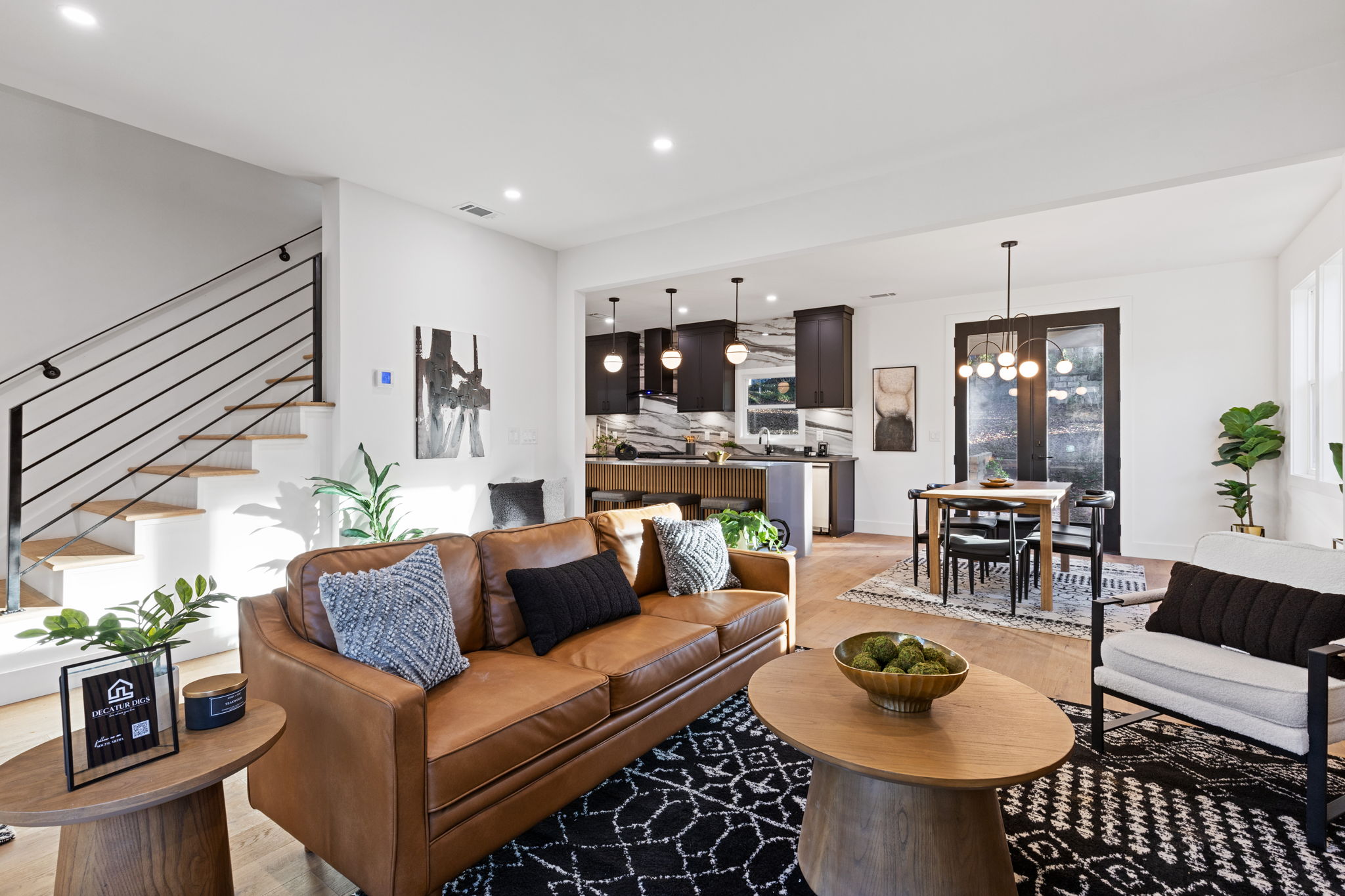 Living room with a tan leather sofa and open stair, looking through to the kitchen and dining area
