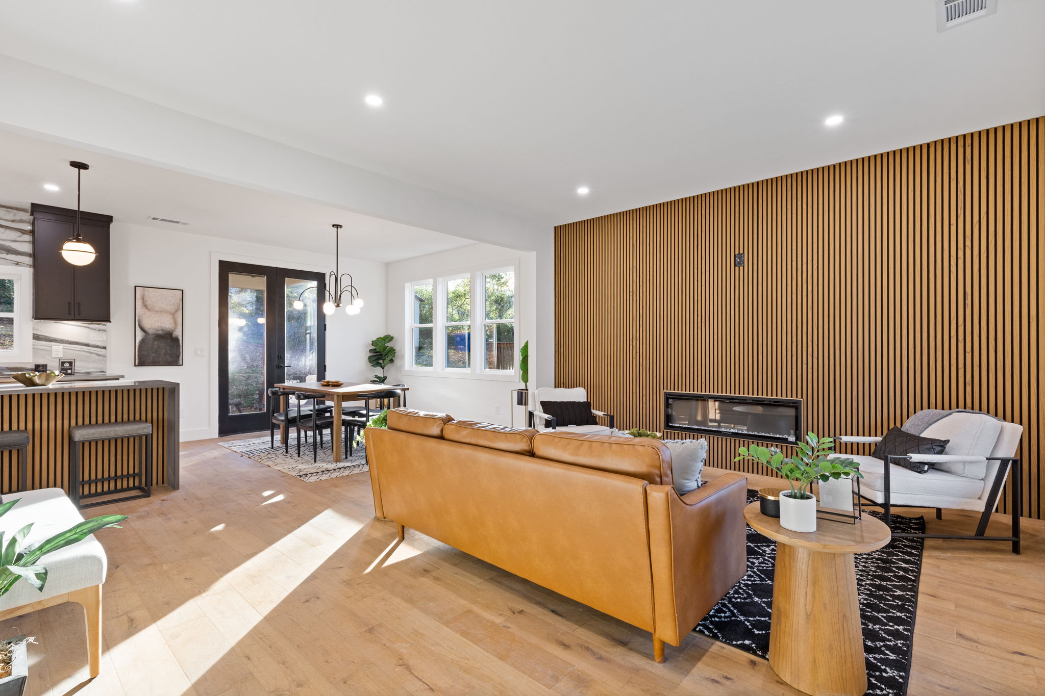 Living and dining area with a wood slat fireplace wall and the open kitchen beyond