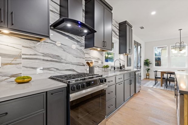 Range wall with a gas range, black hood and marble slab backsplash
