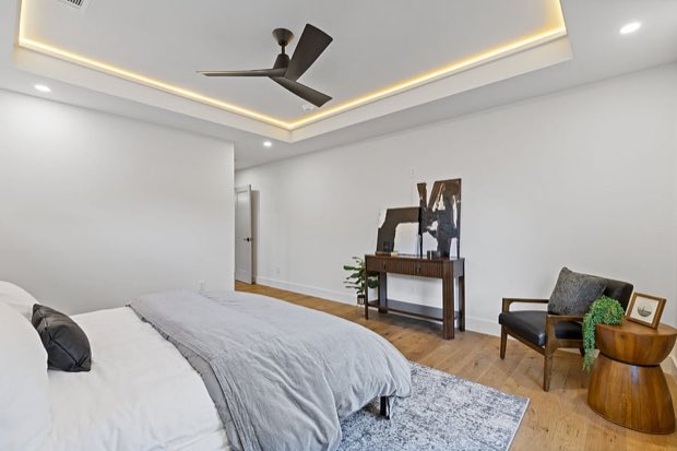 Primary bedroom with a console table, leather chair and tray-ceiling cove lighting