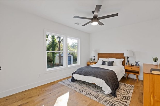 Bedroom with a tan leather headboard, ceiling fan and a window to the trees